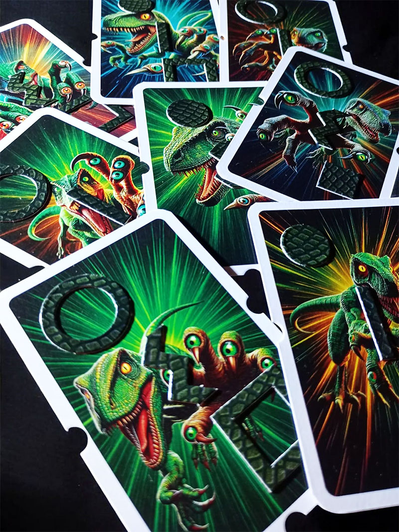 Acercamiento a varias cartas táctiles del juego Velocitactor. Se ven velocitactors ilustrados sobre fondos de colores brillantes y, en relieve, figuras geométricas como círculos, cuadrados y líneas. El ángulo de la foto resalta la textura táctil y las muescas en los bordes que permiten distinguir los mazos.